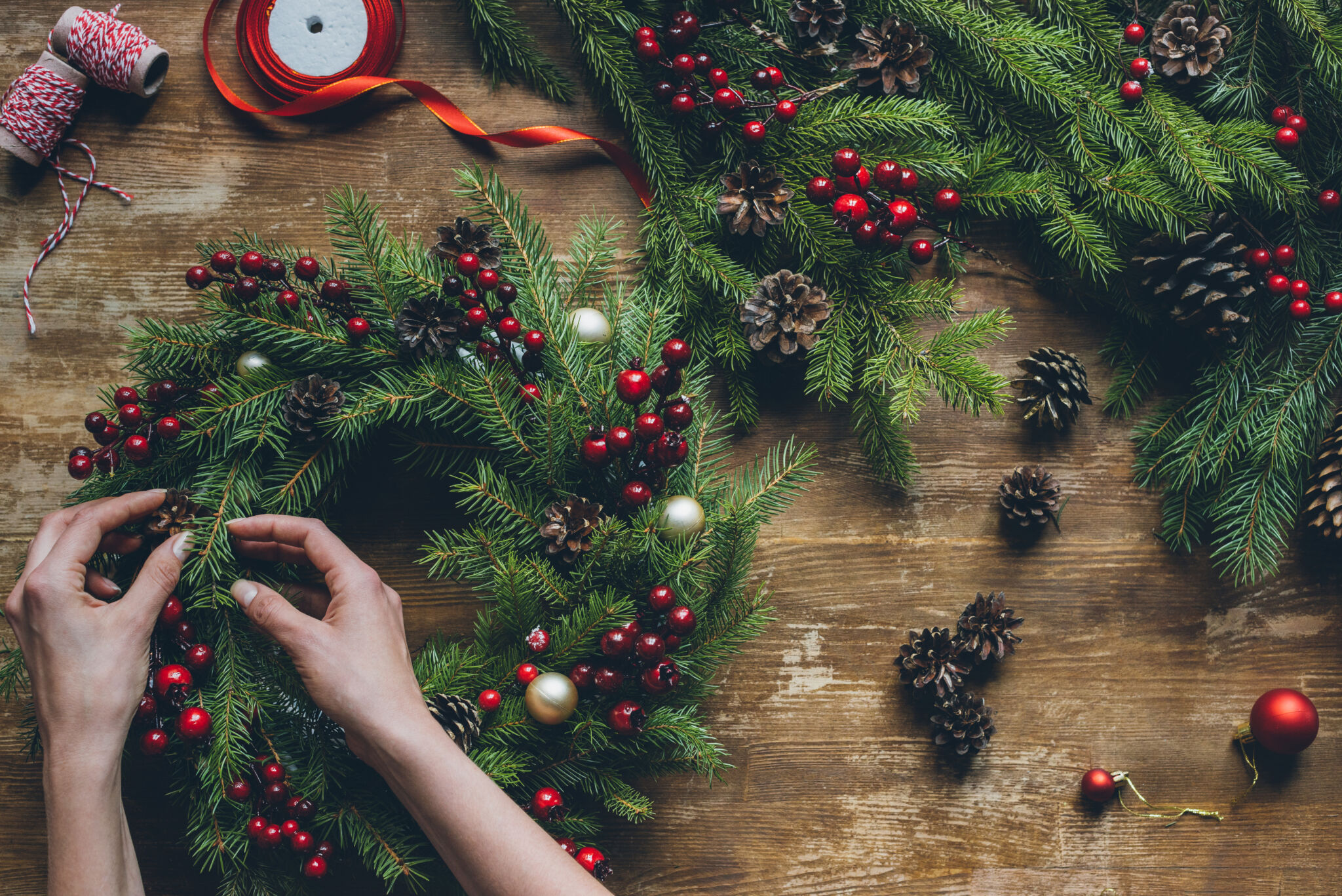top view of florist hands making Christmas wreath on wooden tabletop