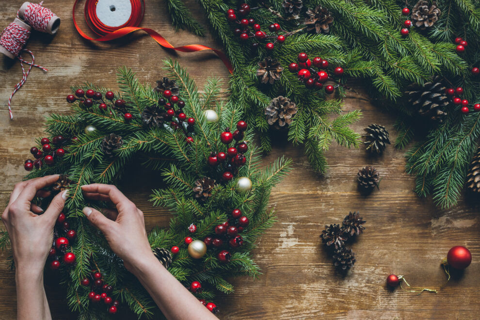 top view of florist hands making Christmas wreath on wooden tabletop