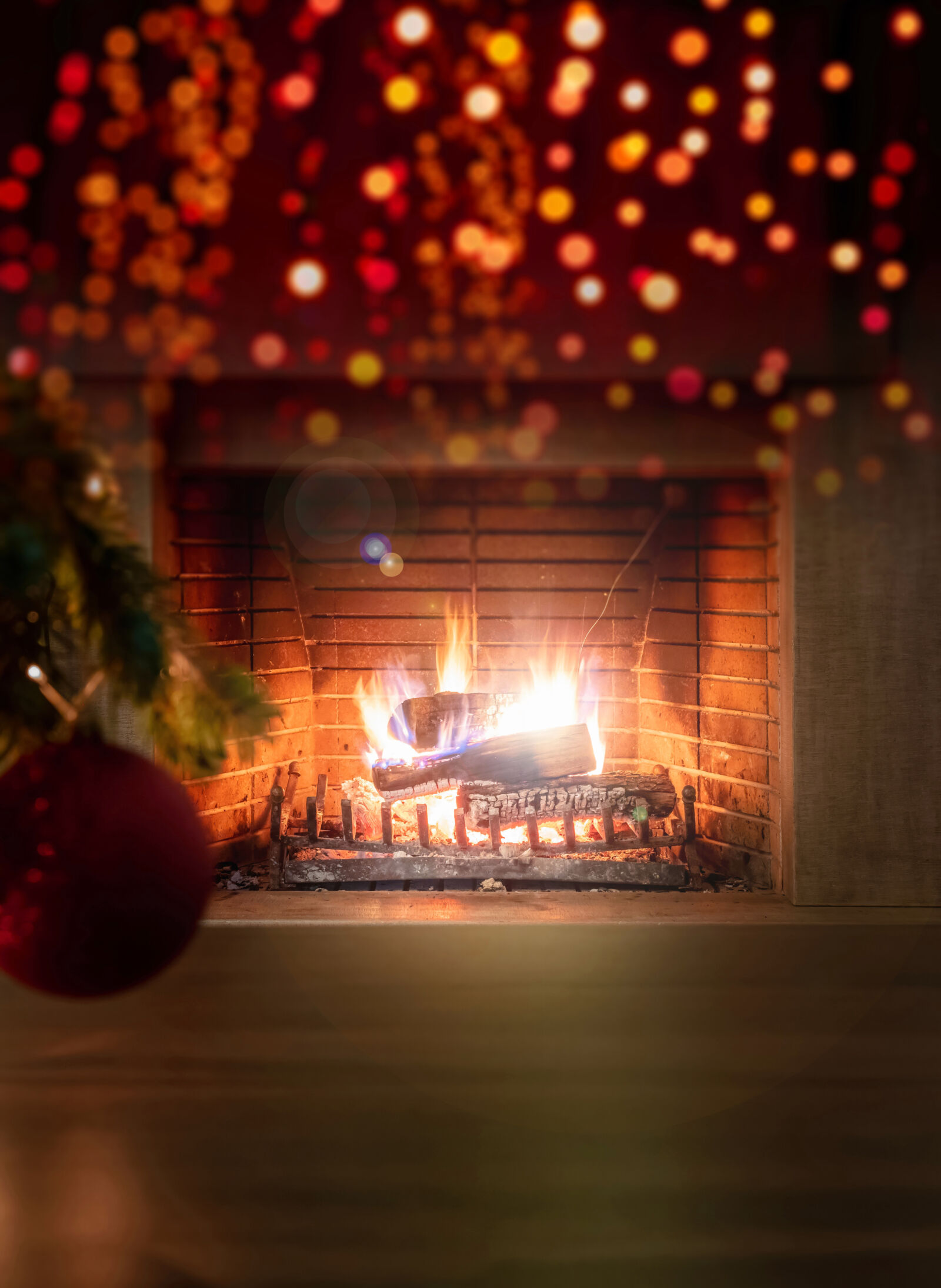 Christmas tree branch with red sparkle ball, bokeh burning fireplace, flames at firewood background, copy space. Warm family moments. Xmas interior home celebration concept.